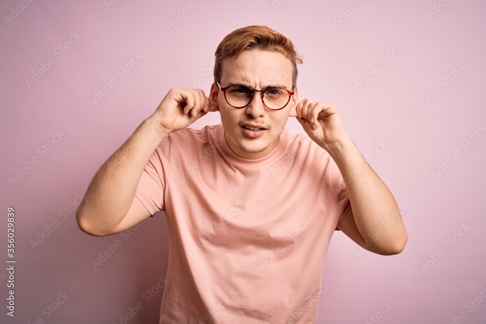 Young handsome redhead man wearing casual t-shirt standing over isolated pink background Smiling pulling ears with fingers, funny gesture. Audition problem Young handsome redhead man wearing casual t-shirt standing over isolated pink background Smiling pulling ears with fingers, funny gesture. Audition problem