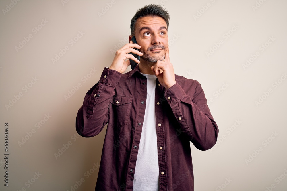 Young handsome man having conversation talking on the smartphone over white background serious face thinking about question, very confused idea Young handsome man having conversation talking on the smartphone over white background serious face thinking about question, very confused idea