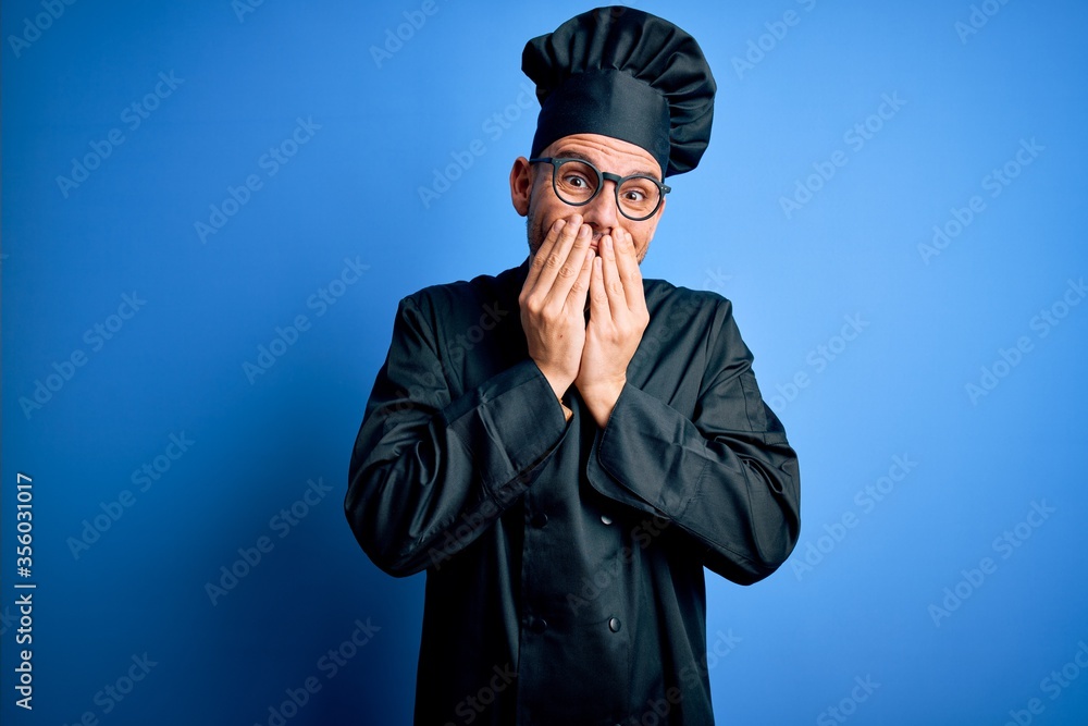 Young handsome chef man wearing cooker uniform and hat over isolated blue background laughing and embarrassed giggle covering mouth with hands, gossip and scandal concept Young handsome chef man wearing cooker uniform and hat over isolated blue background laughing and embarrassed giggle covering mouth with hands, gossip and scandal concept