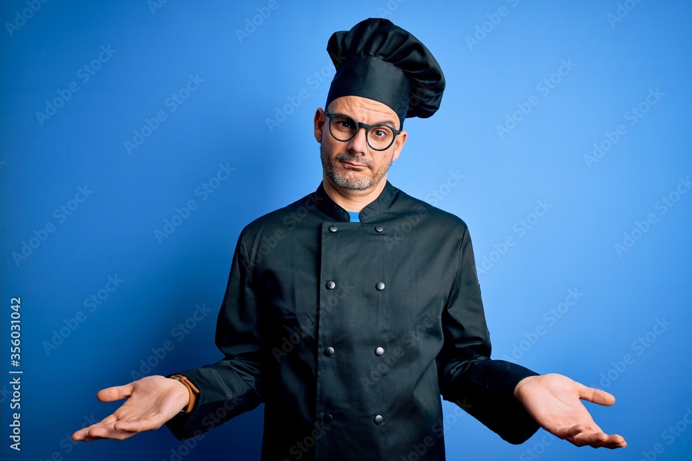 Young handsome chef man wearing cooker uniform and hat over isolated blue background clueless and confused with open arms, no idea concept. Young handsome chef man wearing cooker uniform and hat over isolated blue background clueless and confused with open arms, no idea concept.