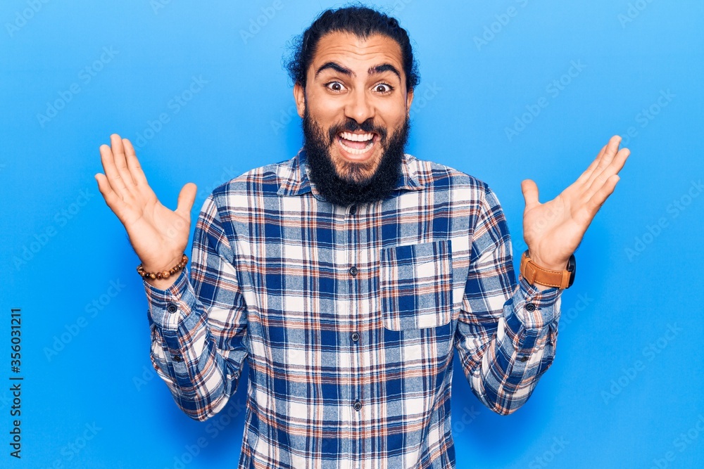 Young arab man wearing casual clothes celebrating victory with happy smile and winner expression with raised hands Young arab man wearing casual clothes celebrating victory with happy smile and winner expression with raised hands