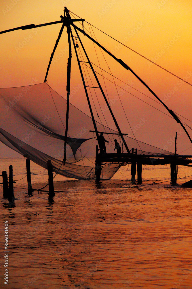 Φωτογραφία silhouette of fisherman fishing with large net during sunset in cochin - india
