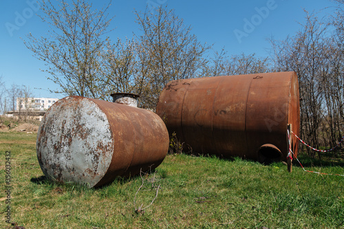 Two old abandoned rusty barrels lie in the open air on the grass