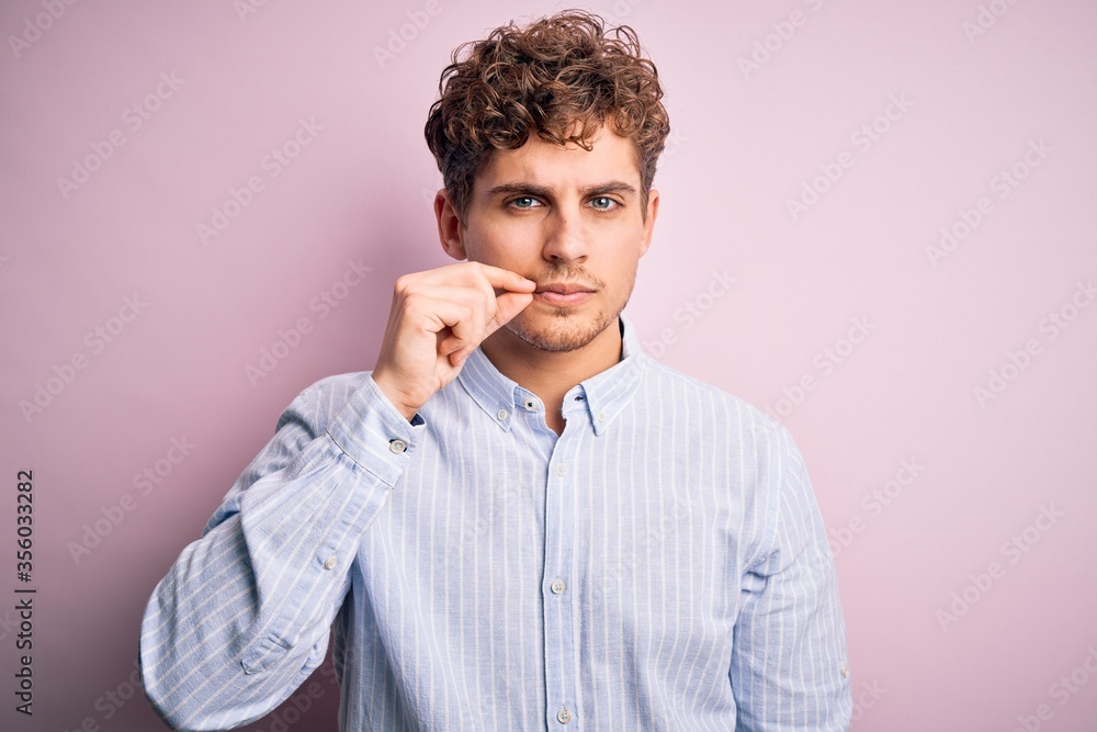 Young blond handsome man with curly hair wearing striped shirt over white background mouth and lips shut as zip with fingers. Secret and silent, taboo talking Young blond handsome man with curly hair wearing striped shirt over white background mouth and lips shut as zip with fingers. Secret and silent, taboo talking