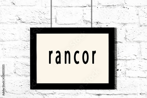 Black frame hanging on white brick wall with inscription rancor
