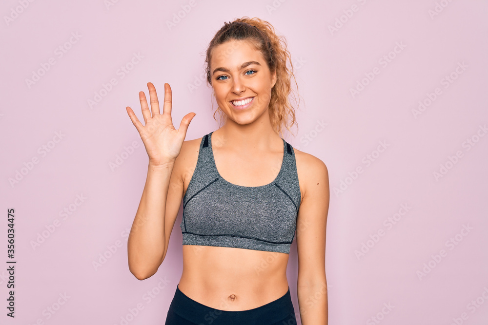 Young beautiful blonde sportswoman with blue eyes doing exercise wearing sportswear showing and pointing up with fingers number five while smiling confident and happy. Young beautiful blonde sportswoman with blue eyes doing exercise wearing sportswear showing and pointing up with fingers number five while smiling confident and happy.