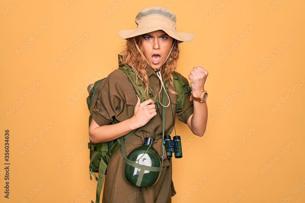 Φωτογραφία Young blonde explorer woman with blue eyes hiking wearing backpack and water canteen angry and mad raising fist frustrated and furious while shouting with anger