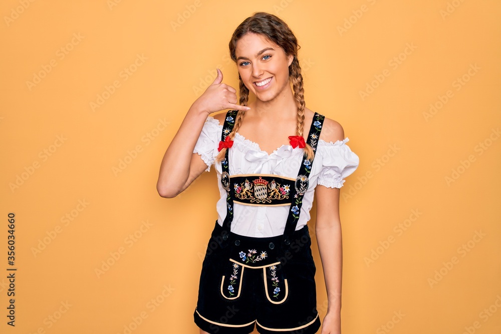 Young beautiful blonde german woman with blue eyes wearing traditional octoberfest dress smiling doing phone gesture with hand and fingers like talking on the telephone. Communicating concepts. Young beautiful blonde german woman with blue eyes wearing traditional octoberfest dress smiling doing phone gesture with hand and fingers like talking on the telephone. Communicating concepts.