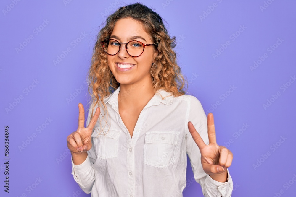 Young beautiful woman with blue eyes wearing casual shirt and glasses over purple background smiling looking to the camera showing fingers doing victory sign. Number two. Young beautiful woman with blue eyes wearing casual shirt and glasses over purple background smiling looking to the camera showing fingers doing victory sign. Number two.