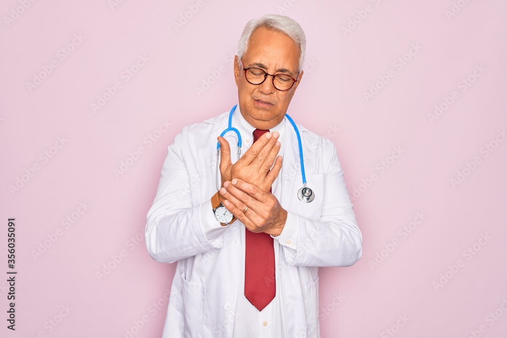 Middle age senior grey-haired doctor man wearing stethoscope and professional medical coat Suffering pain on hands and fingers, arthritis inflammation Middle age senior grey-haired doctor man wearing stethoscope and professional medical coat Suffering pain on hands and fingers, arthritis inflammation