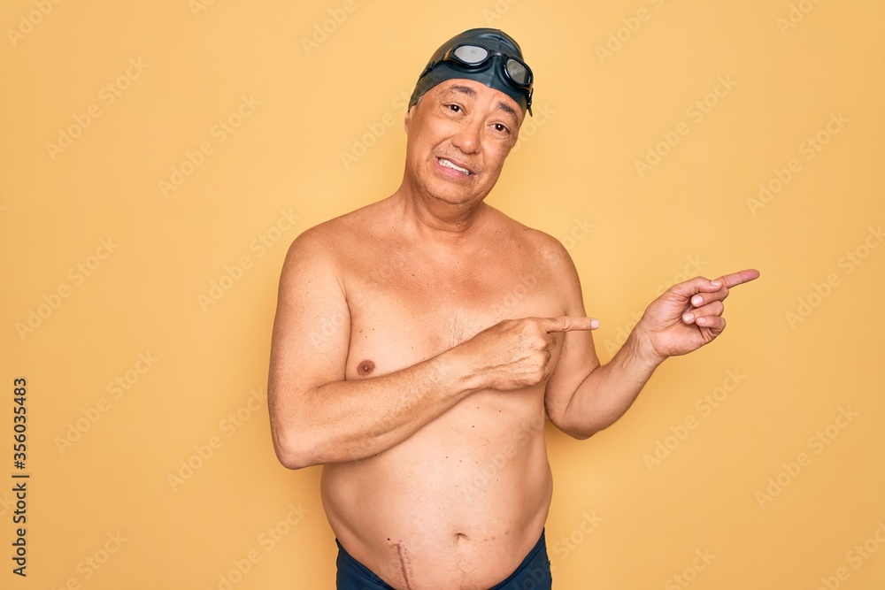 Middle age senior grey-haired swimmer man wearing swimsuit, cap and goggles Pointing aside worried and nervous with both hands, concerned and surprised expression