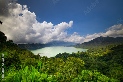 Panoramic landscape. Scenic view to the lake surrounded by hills, mountails and tropical rainforest. Bright sunlight. Buyan lake in Bedugul, Bali, Indonesia © Olga