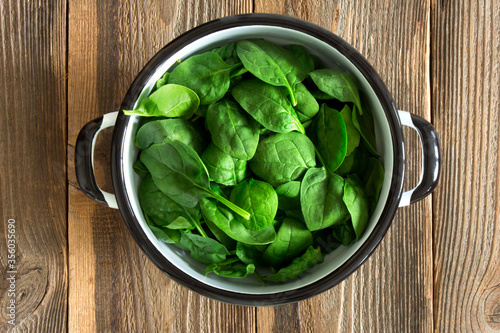 Fresh spinach leaves in a bowl on rustic wooden background.