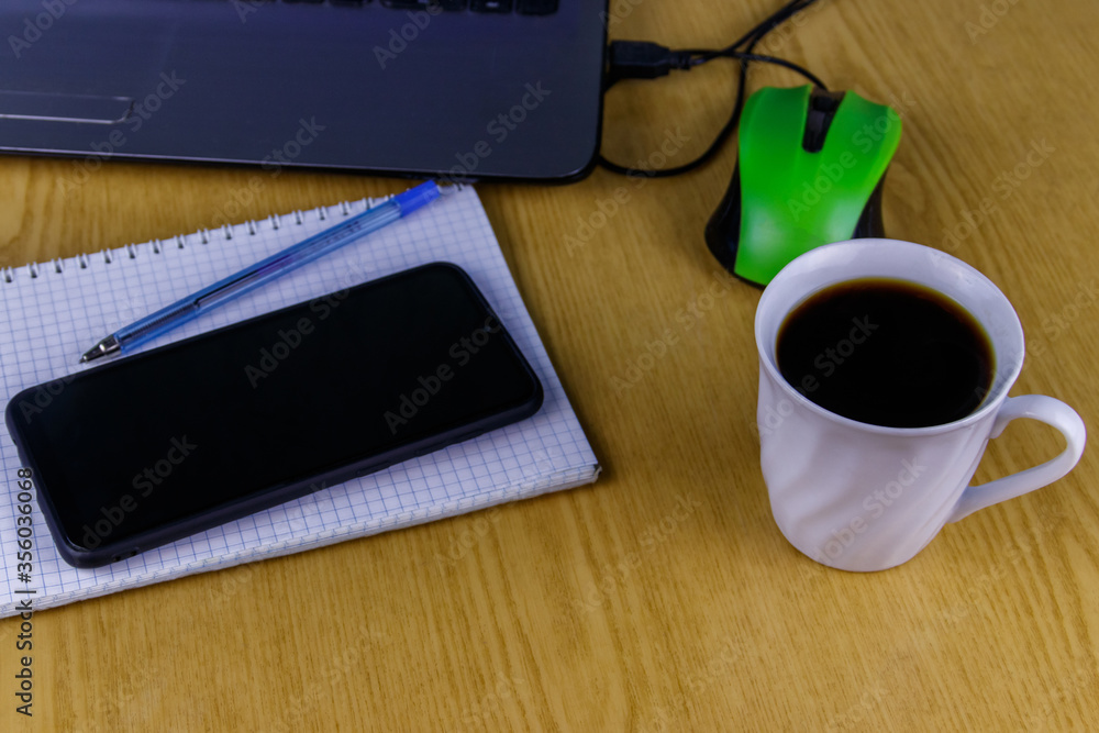 Laptop with mouse, smartphone, notebook, pen and cup of coffee on a desk. Working at home and business concept Laptop with mouse, smartphone, notebook, pen and cup of coffee on a desk. Working at home and business concept