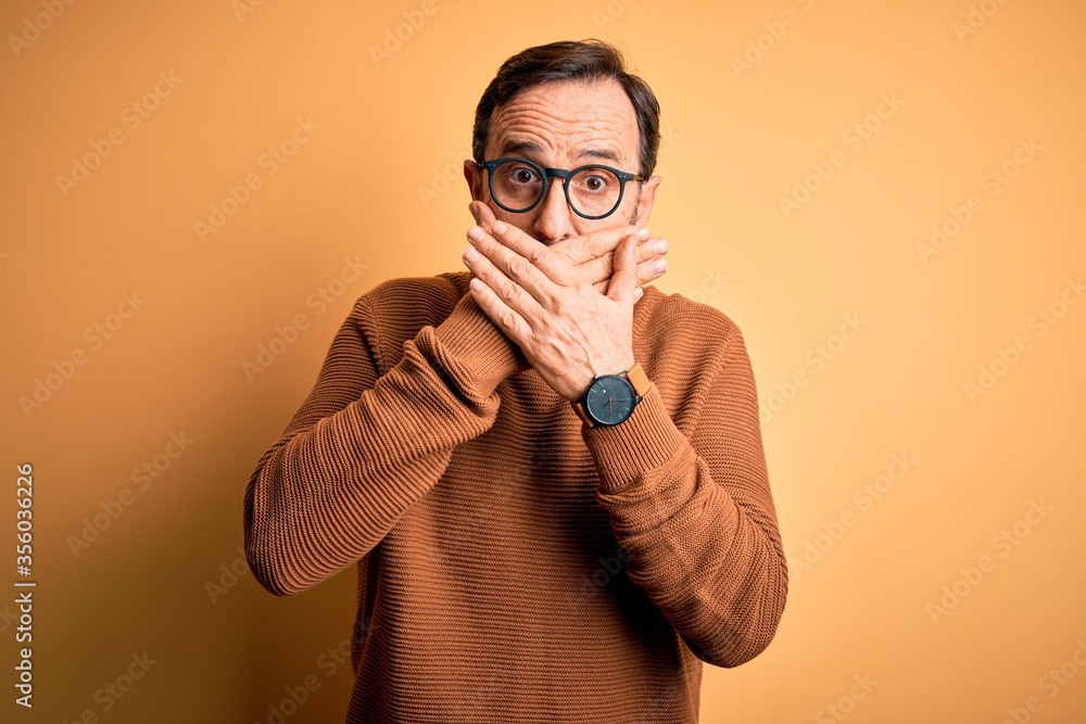 Middle age hoary man wearing brown sweater and glasses over isolated yellow background shocked covering mouth with hands for mistake. Secret concept. Middle age hoary man wearing brown sweater and glasses over isolated yellow background shocked covering mouth with hands for mistake. Secret concept.