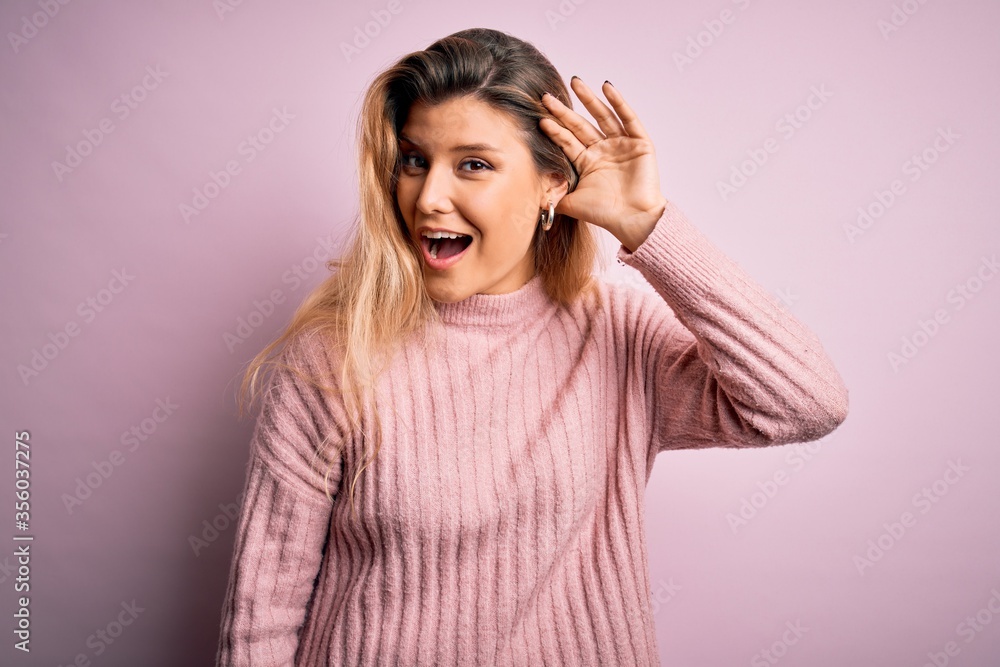 Young beautiful blonde woman wearing casual pink sweater over isolated background smiling with hand over ear listening an hearing to rumor or gossip. Deafness concept. Young beautiful blonde woman wearing casual pink sweater over isolated background smiling with hand over ear listening an hearing to rumor or gossip. Deafness concept.