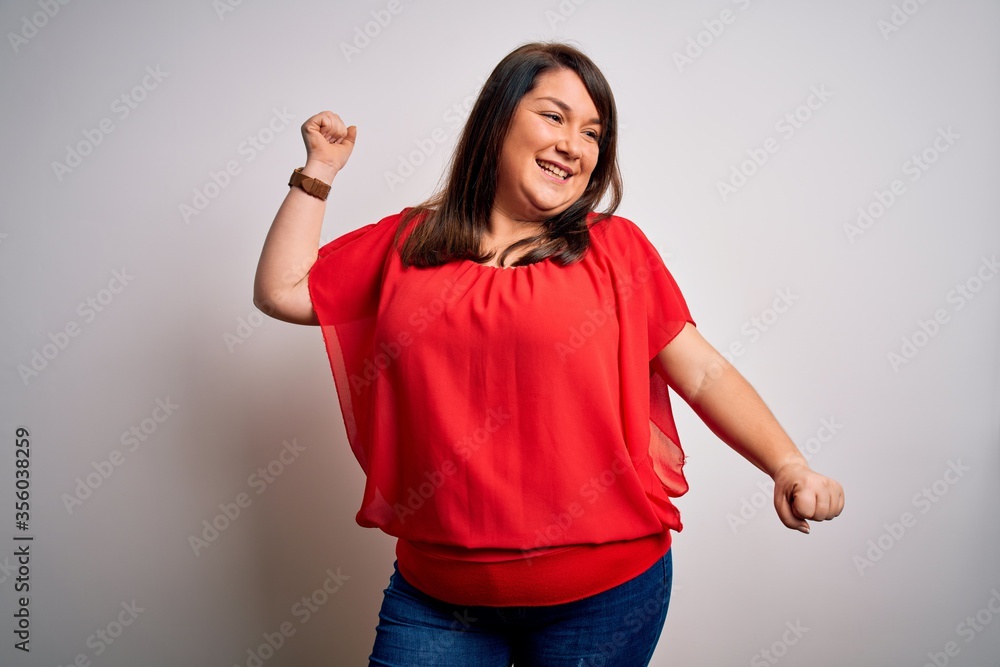 Beautiful brunette plus size woman wearing casual red t-shirt over isolated white background Dancing happy and cheerful, smiling moving casual and confident listening to music Beautiful brunette plus size woman wearing casual red t-shirt over isolated white background Dancing happy and cheerful, smiling moving casual and confident listening to music