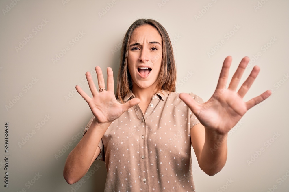 Young beautiful woman wearing casual shirt standing over isolated white background afraid and terrified with fear expression stop gesture with hands, shouting in shock. Panic concept. Young beautiful woman wearing casual shirt standing over isolated white background afraid and terrified with fear expression stop gesture with hands, shouting in shock. Panic concept.