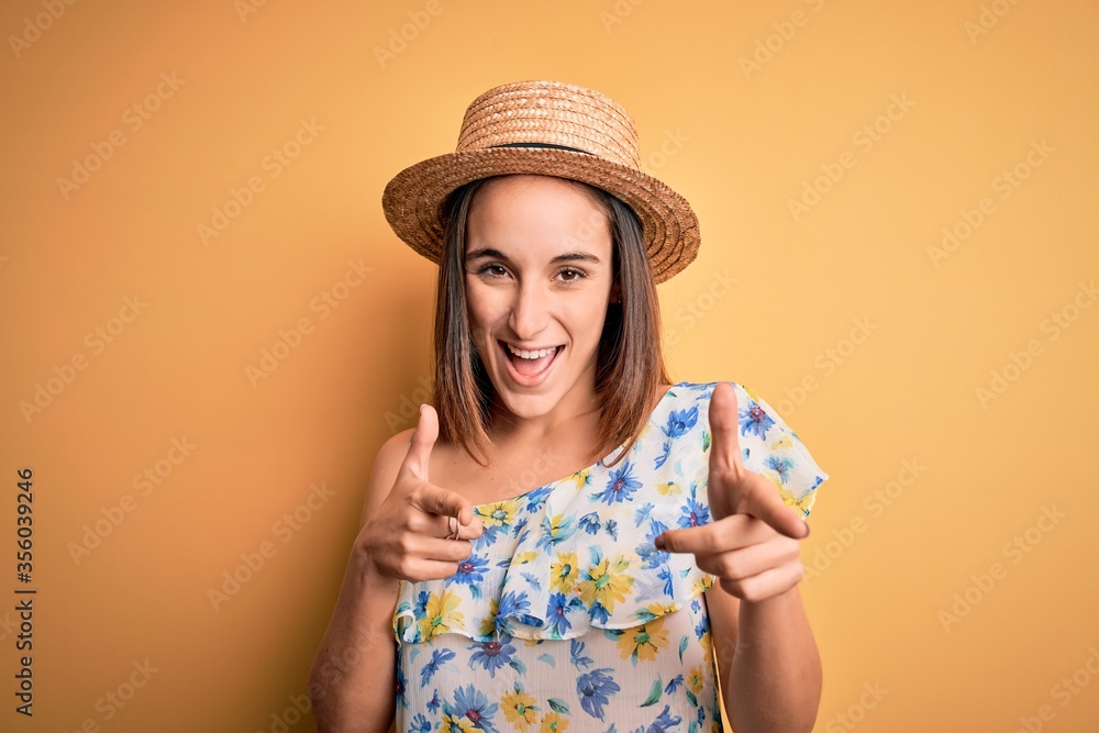 Young beautiful woman wearing casual t-shirt and summer hat over isolated yellow background pointing fingers to camera with happy and funny face. Good energy and vibes. Young beautiful woman wearing casual t-shirt and summer hat over isolated yellow background pointing fingers to camera with happy and funny face. Good energy and vibes.