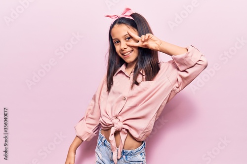 Beautiful child girl wearing casual clothes doing peace symbol with fingers over face, smiling cheerful showing victory