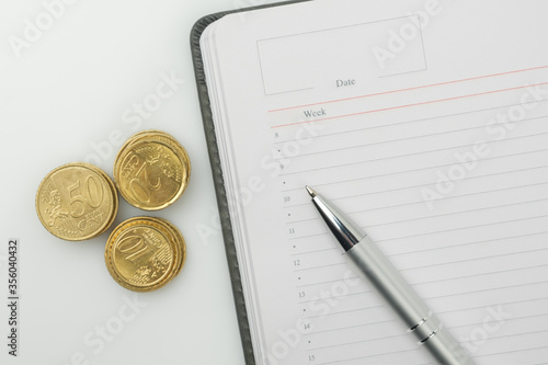 Coins, blank notepad and pen on a white background.
