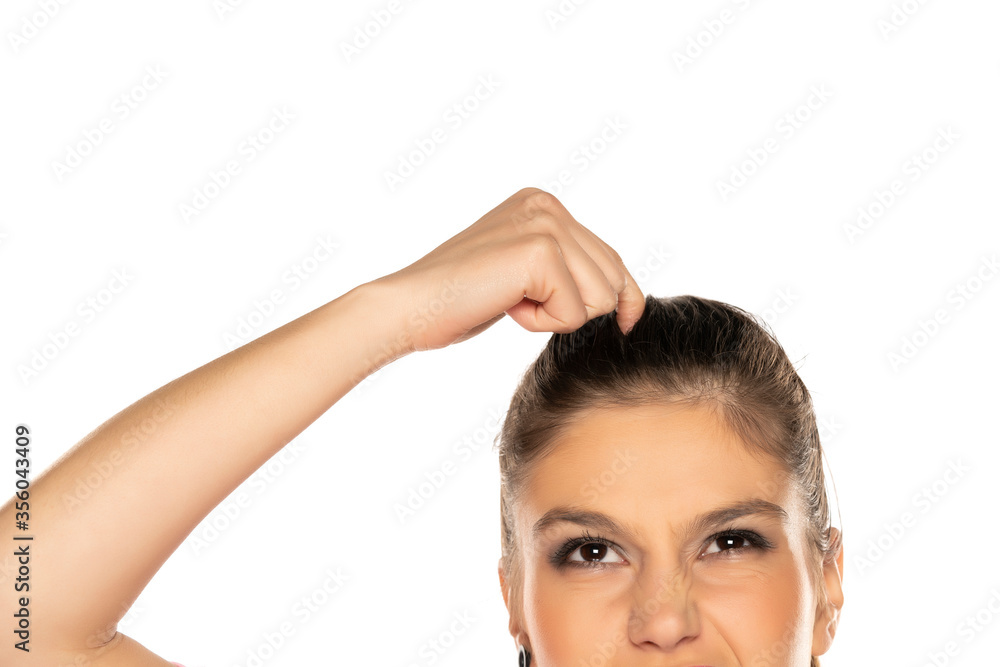 portrait of young nervous woman scratches her head on white background