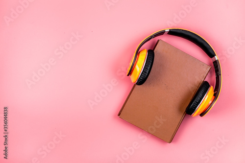 Book and yellow headphones on. Pink background top view copy space