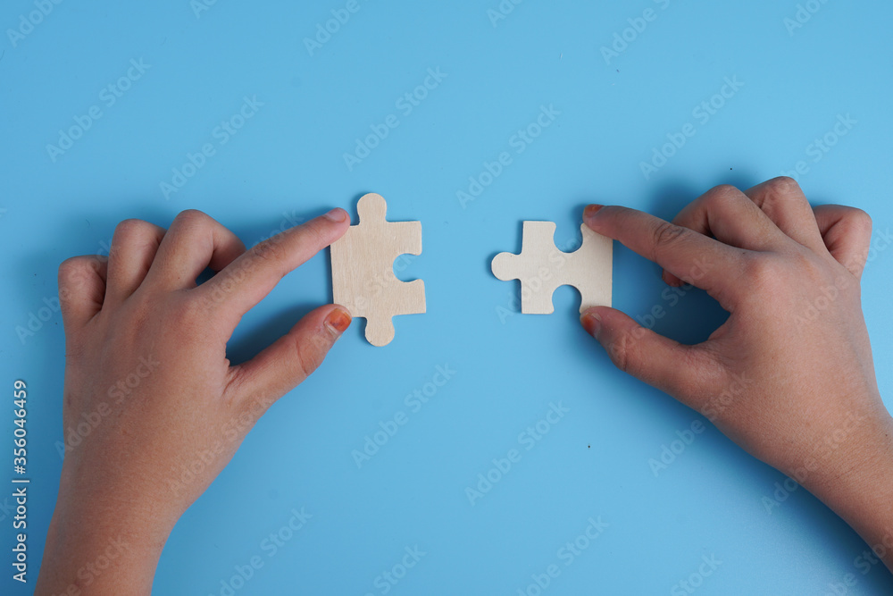 Child's hands holding two puzzle pieces on blue background as a symbol of autism awareness.
Child's hands holding two puzzle pieces on blue background as a symbol of autism awareness.