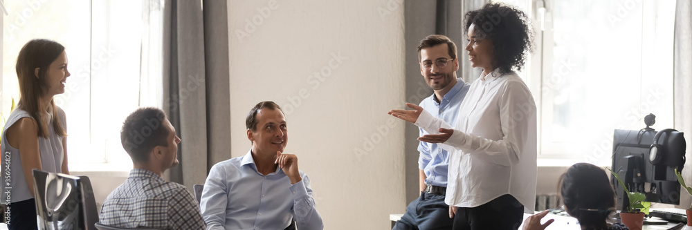 African team leader talking to colleagues at modern office during meeting. Employees listen speaker new ideas, goals at corporate briefing training. Horizontal photo banner for website header design African team leader talking to colleagues at modern office during meeting. Employees listen speaker new ideas, goals at corporate briefing training. Horizontal photo banner for website header design
