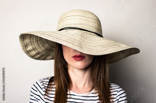 Young woman in a hat. Face is covered hat. Fashion studio portrait.