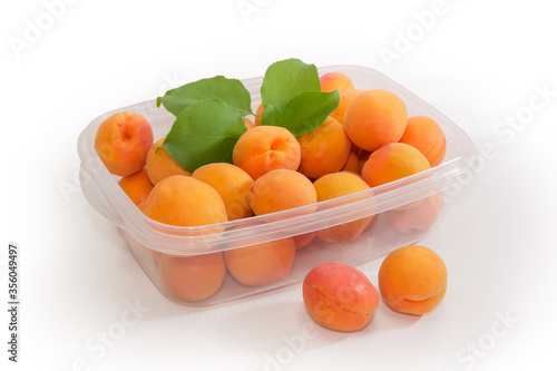 Ripe apricots in plastic food container on the light surface
