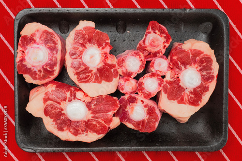 Konstfotografi Fresh raw beef ox tail cuts on a black plastic trey and red and white butcher apron