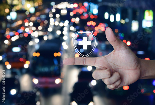 Cross shape with shield flat icon on finger over blur colorful night light traffic jam road with cars in city, Business healthy and medical care insurance concept