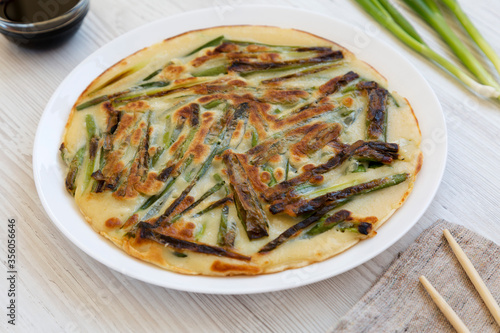 Homemade korean Pajeon scallion pancake on a white plate on a white wooden table, side view. Asian food. Close-up.