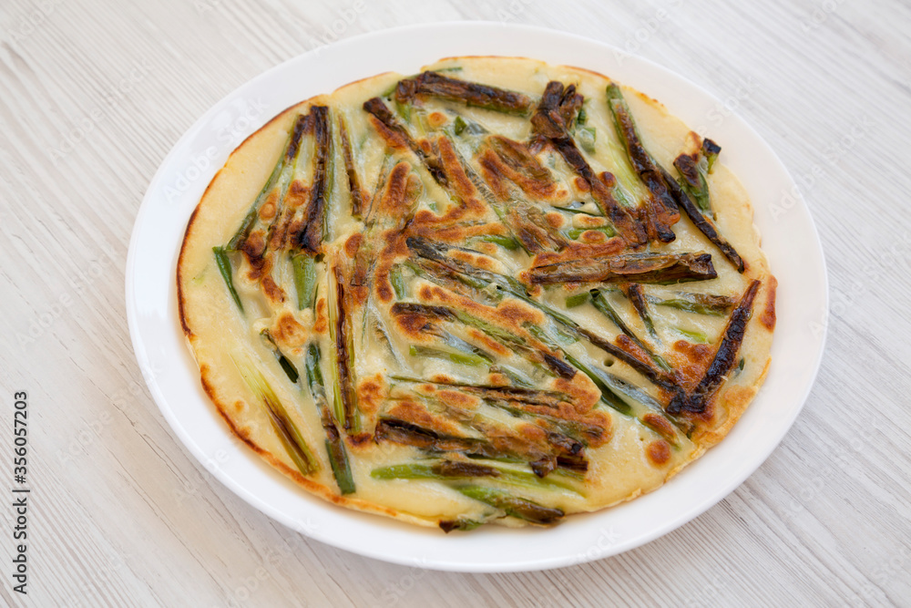 Homemade korean Pajeon scallion pancake on a white plate on a white wooden table, side view. Asian food. Close-up. Homemade korean Pajeon scallion pancake on a white plate on a white wooden table, side view. Asian food. Close-up.