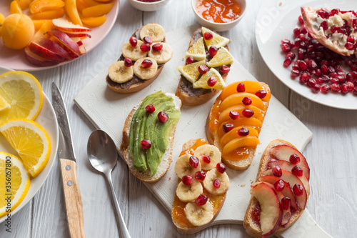 Process of making sweet toast with jam and various fruits apricots, peaches, bananas, oranges and avocado decorated with pomegranates on top.