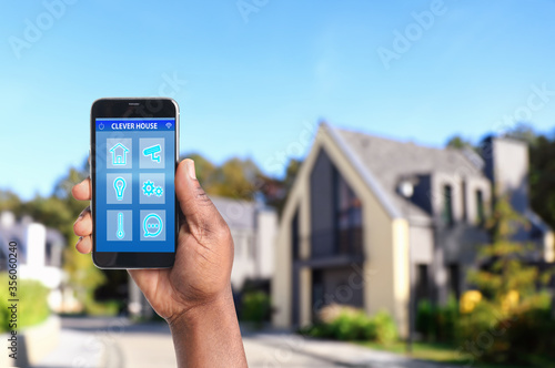 African-American man using home security app on smartphone outdoors, closeup. Space for text