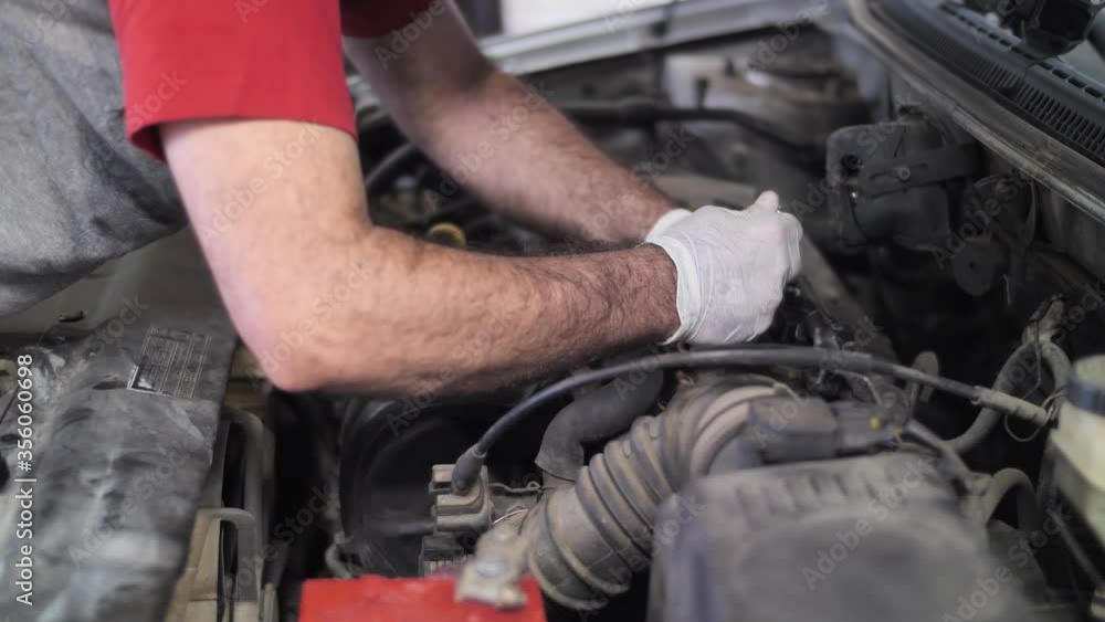 Mechanic at work, repairing car engine on open hood, oil changing procedure Mechanic at work, repairing car engine on open hood, oil changing procedure