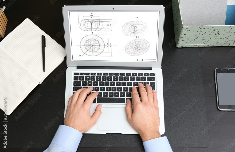 Male engineer working with technical drawing on laptop at table, top view Male engineer working with technical drawing on laptop at table, top view