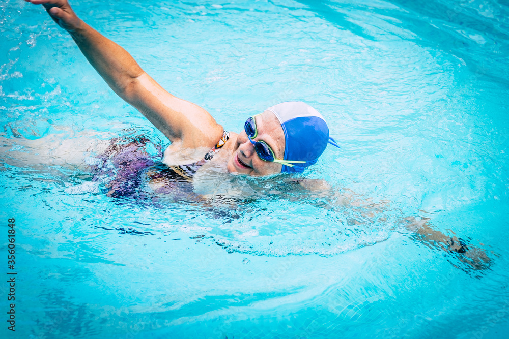 Elderly woman in activity swimming in the outdoor turquoise swimming pool.  With swimming cap and goggles. Healthy lifestyle retirement concept