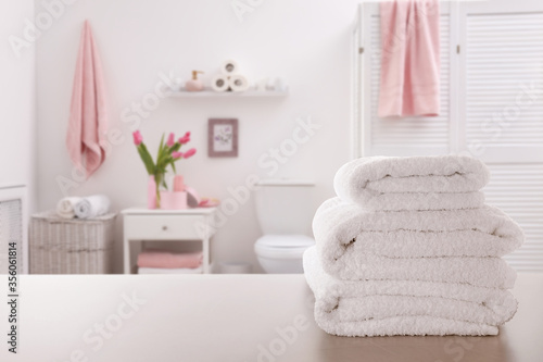 Stack of fresh towels on light grey table in bathroom. Space for text