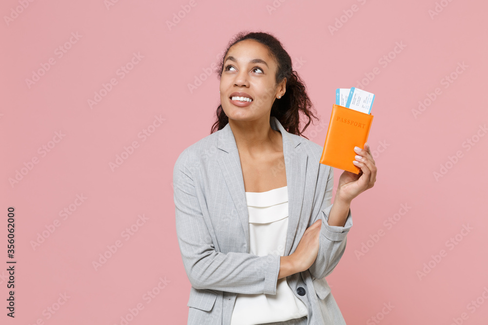 Pensive young african american business woman in grey suit white shirt posing isolated on pink background. Achievement career wealth business concept. Hold passport tickets boarding pass, looking up. Pensive young african american business woman in grey suit white shirt posing isolated on pink background. Achievement career wealth business concept. Hold passport tickets boarding pass, looking up.
