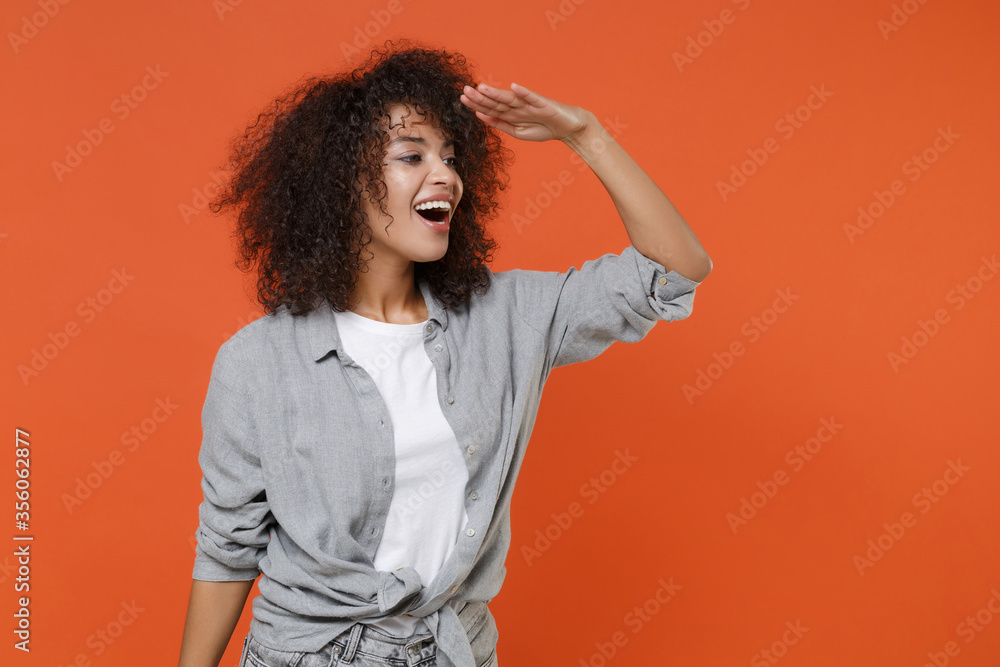 Excited young african american woman girl in gray casual clothes isolated on orange background studio. People lifestyle concept. Mock up copy space. Holding hand at forehead looking far away distance. Excited young african american woman girl in gray casual clothes isolated on orange background studio. People lifestyle concept. Mock up copy space. Holding hand at forehead looking far away distance.