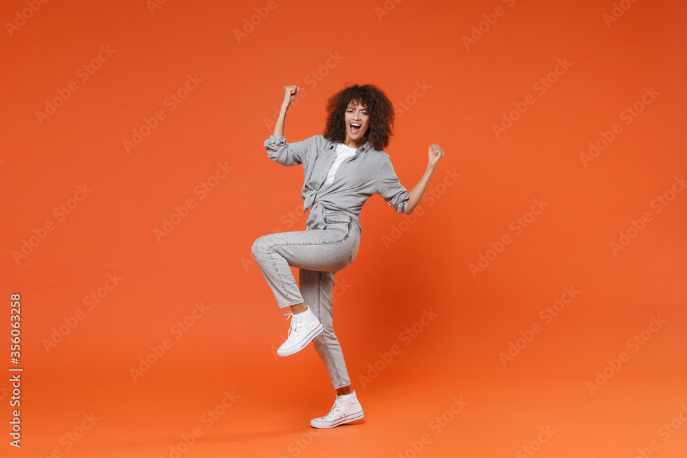 Joyful young african american woman girl in casual clothes posing isolated on orange background studio portrait. People sincere emotions lifestyle concept. Mock up copy space. Doing winner gesture.