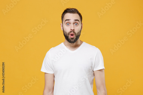 Shocked young bearded man guy in white casual t-shirt posing isolated on yellow wall background studio portrait. People sincere emotions lifestyle concept. Mock up copy space. Keeping mouth open.