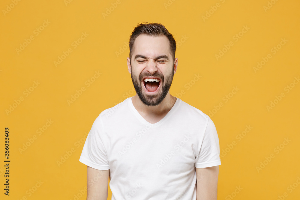 Crazy young bearded man guy in white casual t-shirt posing isolated on yellow background studio portrait. People sincere emotions lifestyle concept. Mock up copy space. Keeping eyes closed, screaming. Crazy young bearded man guy in white casual t-shirt posing isolated on yellow background studio portrait. People sincere emotions lifestyle concept. Mock up copy space. Keeping eyes closed, screaming.