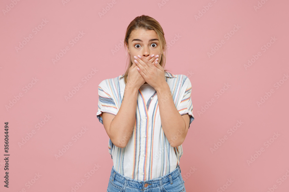 Shocked young blonde woman girl in casual striped shirt posing isolated on pastel pink background studio portrait. People emotions lifestyle concept. Mock up copy space. Covering mouth with hands. Shocked young blonde woman girl in casual striped shirt posing isolated on pastel pink background studio portrait. People emotions lifestyle concept. Mock up copy space. Covering mouth with hands.