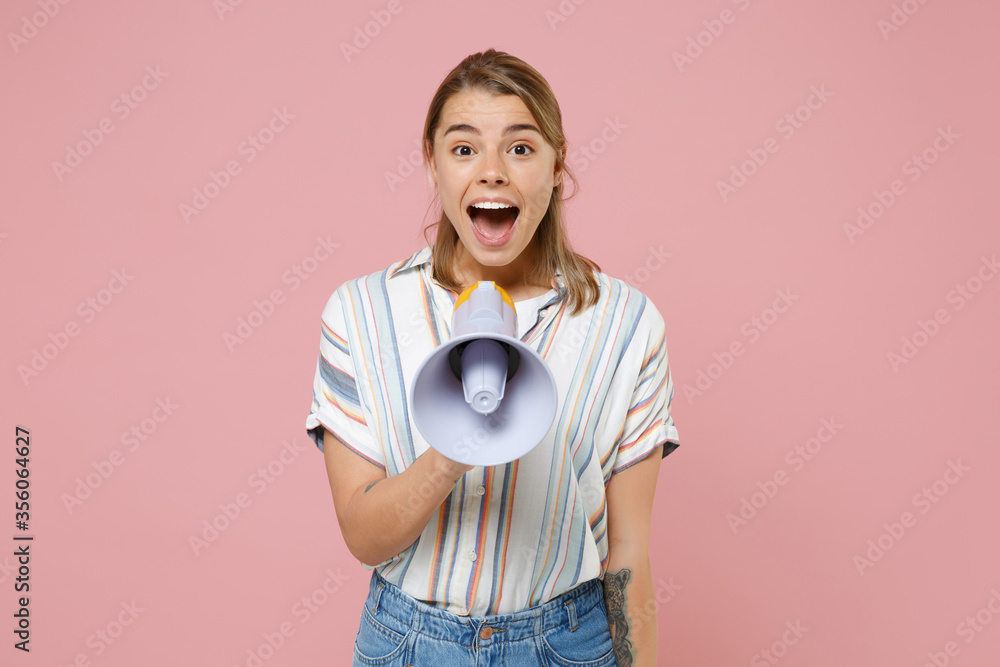 Surprised young blonde woman girl in casual striped shirt posing isolated on pastel pink wall background studio portrait. People emotions lifestyle concept. Mock up copy space. Screaming in megaphone. Surprised young blonde woman girl in casual striped shirt posing isolated on pastel pink wall background studio portrait. People emotions lifestyle concept. Mock up copy space. Screaming in megaphone.