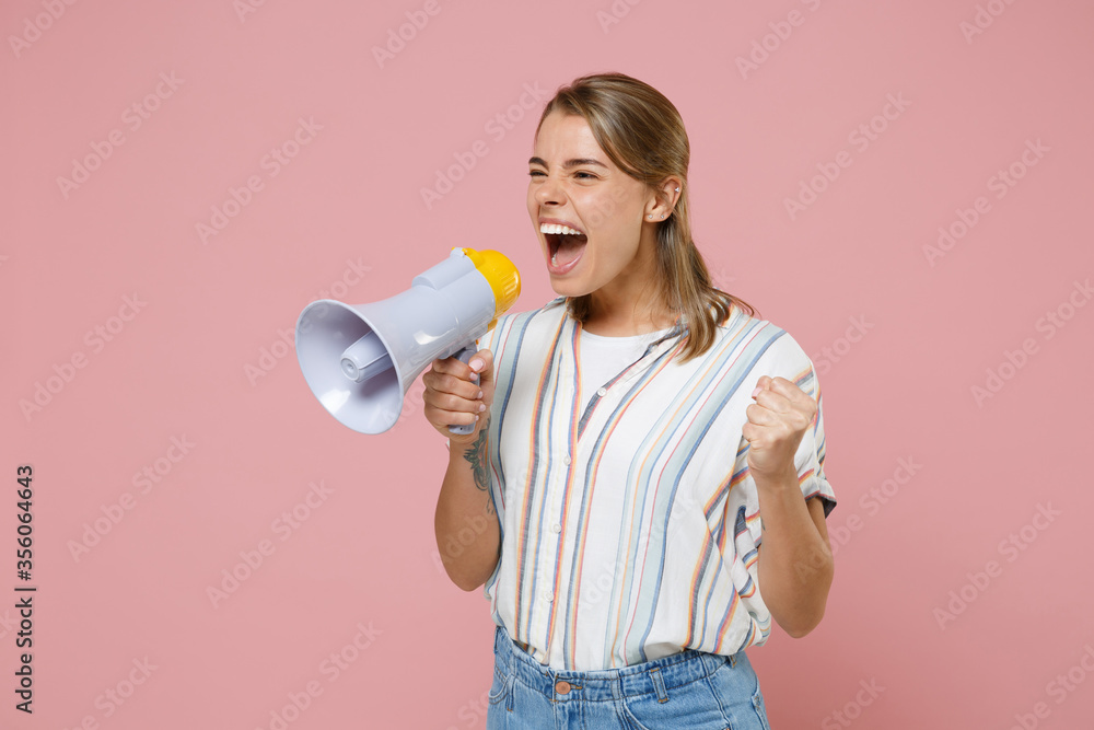 Crazy young blonde woman girl in casual striped shirt posing isolated on pastel pink background studio portrait. People lifestyle concept. Mock up copy space. Screaming in megaphone, clenching fist. Crazy young blonde woman girl in casual striped shirt posing isolated on pastel pink background studio portrait. People lifestyle concept. Mock up copy space. Screaming in megaphone, clenching fist.