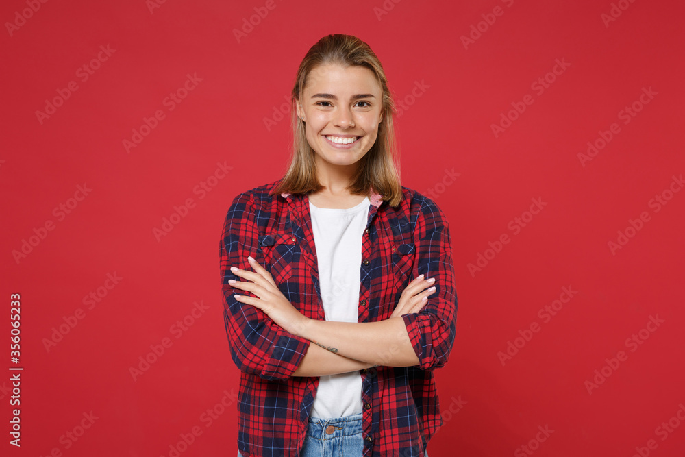 Smiling young blonde woman girl in casual checkered shirt posing isolated on red wall background studio portrait. People sincere emotions lifestyle concept. Mock up copy space. Holding hands crossed. Smiling young blonde woman girl in casual checkered shirt posing isolated on red wall background studio portrait. People sincere emotions lifestyle concept. Mock up copy space. Holding hands crossed.